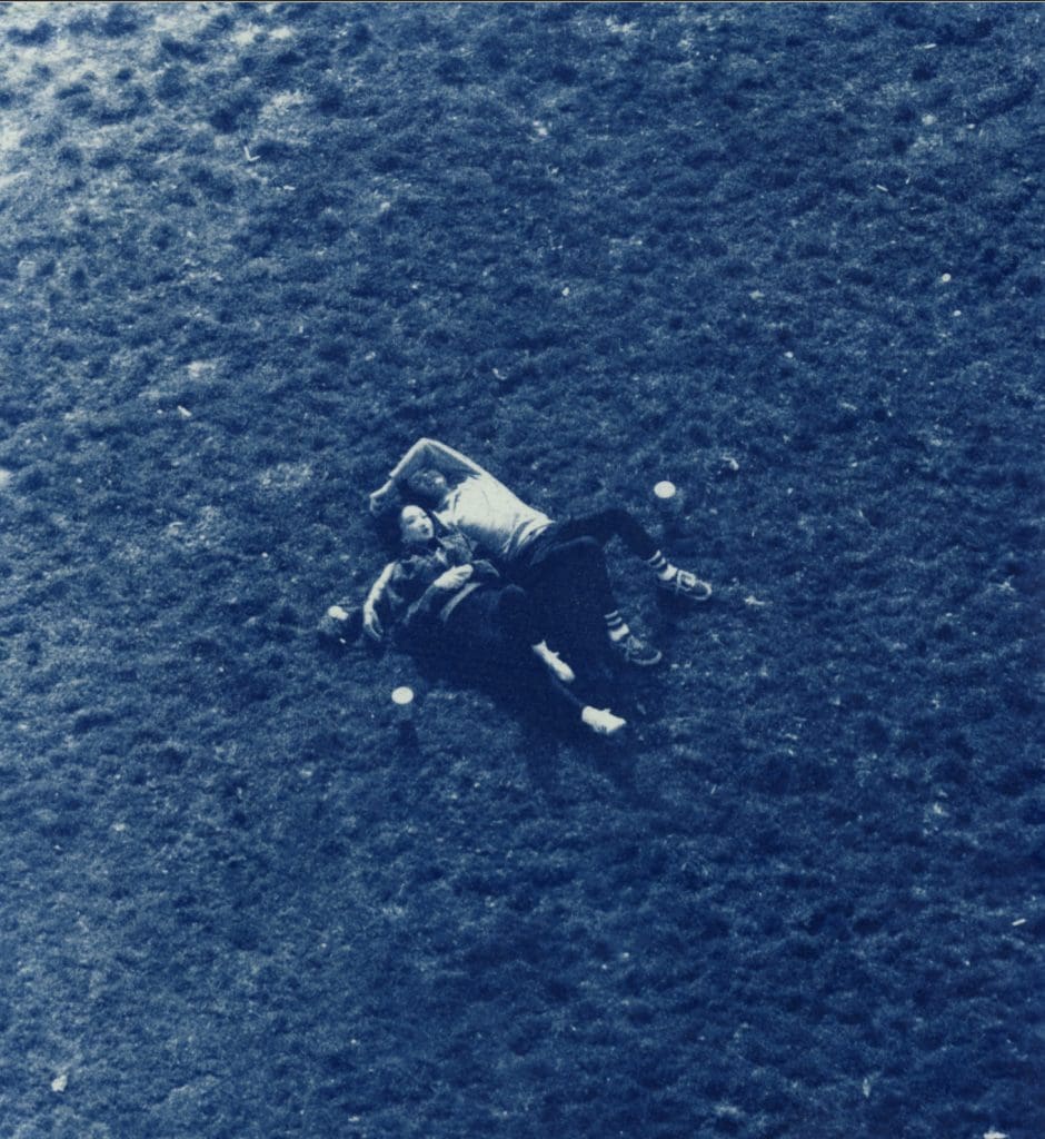 color cyanotype image of two people laying in a grass field